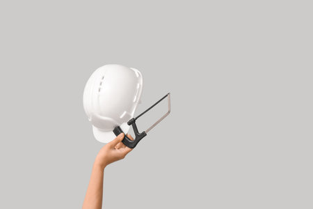Hands with hardhat and hacksaw on gray backgroundの写真素材