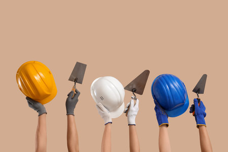 Hands with hardhats and masonry trowels on beige backgroundの写真素材