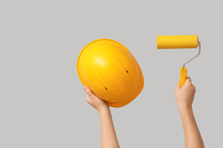 Hands with hardhat and paint roller on gray backgroundの写真素材