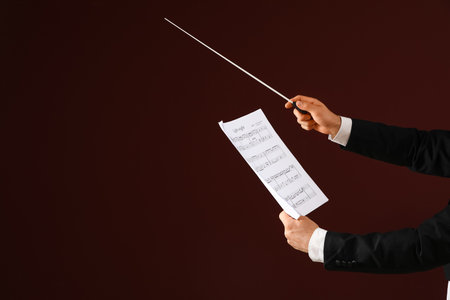 Hands of male conductor with baton and note sheet on brown backgroundの写真素材