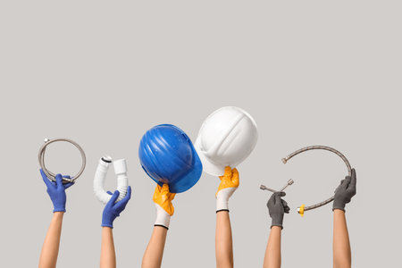Hands with hardhat and plumber supplies on gray backgroundの写真素材