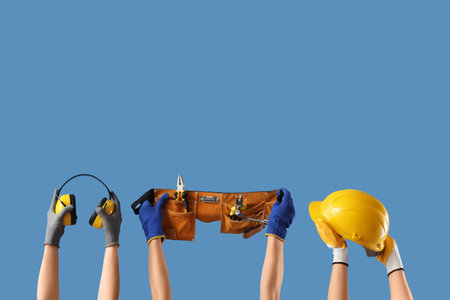 Hands with hardhat, tool belt and protective earmuffs on blue backgroundの写真素材