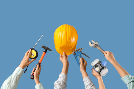 Hands with hardhat and construction tools on blue background