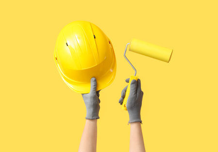 Hands with hardhat and paint roller on yellow backgroundの写真素材