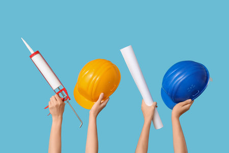 Hands with hardhats, blueprint and sealant on blue backgroundの写真素材