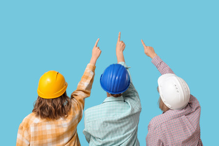 Women in hardhats pointing at something on blue background, back viewの写真素材