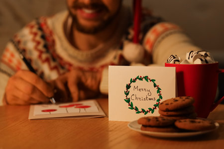 Christmas greeting card with cookies and cocoa against man writing on table at home, closeupの写真素材