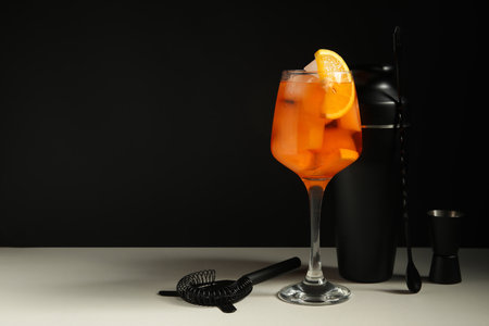 Glass of Aperol spritz cocktail and bartender tools on white table near black wall, closeupの写真素材