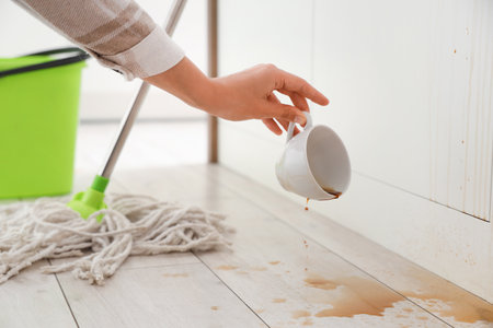 Woman picking up overturned cup of coffee from floor in kitchenの写真素材