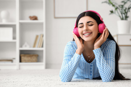 Beautiful young woman in modern headphones listening to music at homeの写真素材