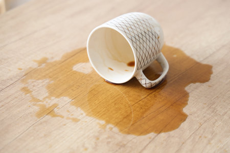 Overturned cup and spilled coffee on table in kitchen, closeupの写真素材