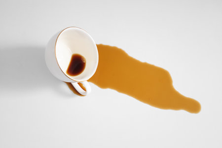 Overturned cup and spilled coffee on table in kitchen, closeupの写真素材