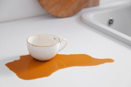 Cup and spilled coffee on table in kitchenの写真素材