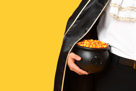 Young man dressed as vampire for Halloween with cauldron of candy corns on yellow background, closeupの写真素材