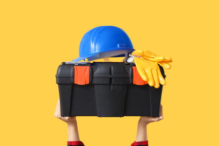 Hands with hardhat and tool box on yellow backgroundの写真素材