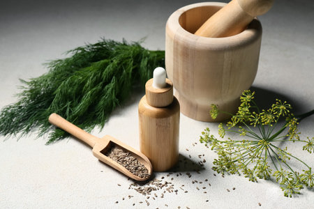 Bottle of dill oil with seeds and mortar on gray grunge background
