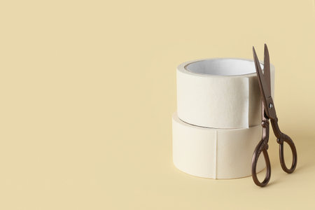 Rolls of white masking tape with scissors on beige backgroundの写真素材