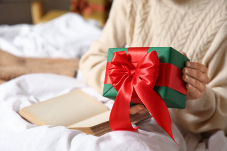 Woman with beautiful Christmas gift box and book in bedroom, closeupの写真素材