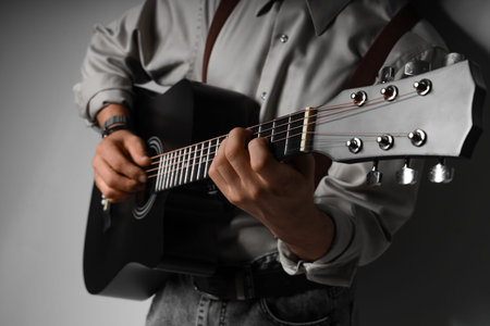 Young man playing acoustic guitar on gray background