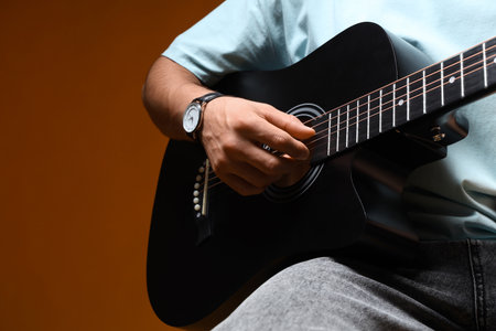Young man playing acoustic guitar on yellow backgroundの写真素材