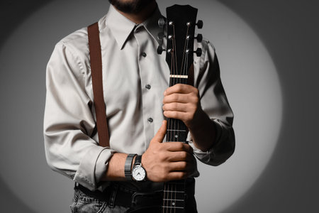 Young man with guitar on gray background