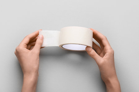 Female hands with roll of white masking tape on gray backgroundの写真素材