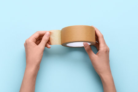 Female hands with roll of brown masking tape on blue backgroundの写真素材