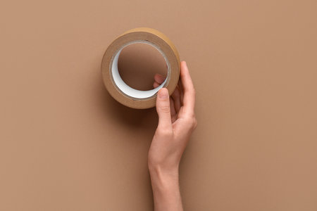 Female hand with roll of masking tape on brown backgroundの写真素材
