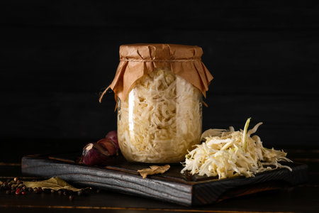 Jar with tasty sauerkraut and different spices on black wooden backgroundの写真素材