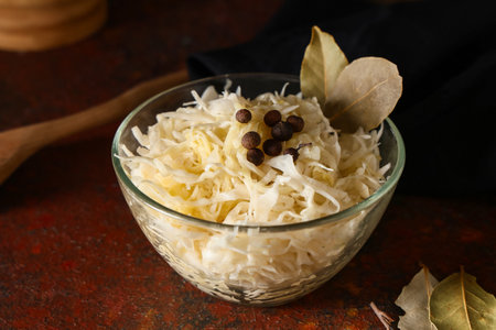 Glass bowl with tasty sauerkraut, peppercorns and bay leaves on dark background, closeupの写真素材