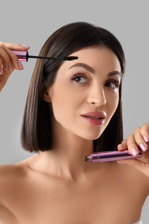 Beautiful young woman with mascara on light background, closeup