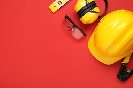 Hardhats, safety glasses and protective earmuffs on red background