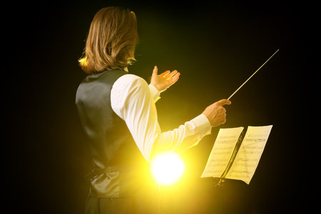 Young male conductor with note sheets on dark backgroundの写真素材