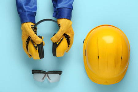 Hands of worker with hardhat, protective earmuffs and safety glasses on blue backgroundの写真素材