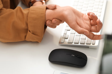 Woman suffering from pain in wrist at table in officeの写真素材