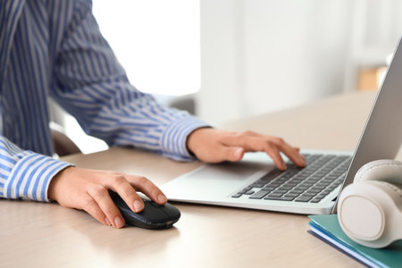 Hands of woman using computer mouse and laptop at table in officeの写真素材