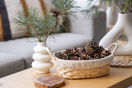 Basket with coniferous cones and pine tree branches on table in living roomの写真素材