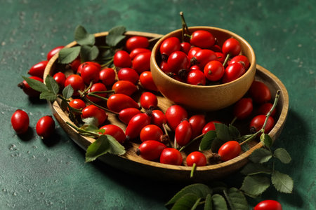 Wooden plate an bowl with fresh rose hip berries on green background, closeupの写真素材