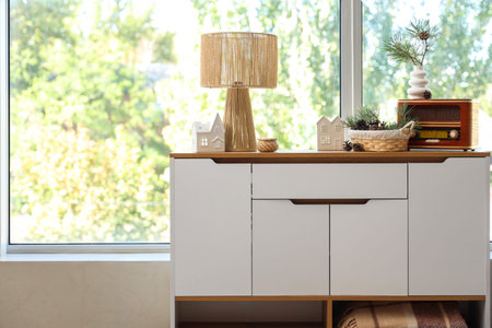 Basket with coniferous cones and retro radio receiver and lamp on commode near window in roomの写真素材