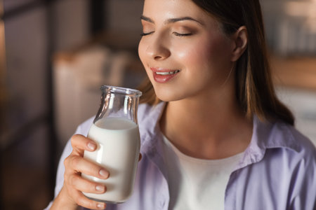Young woman with glass bottle of milk in kitchen at night, closeupの写真素材