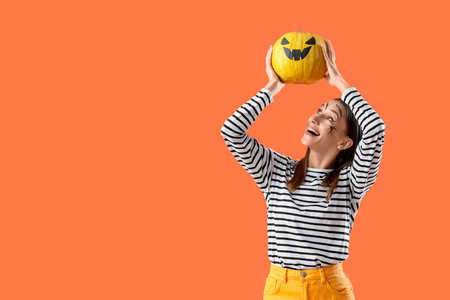 Beautiful young happy woman with Halloween pumpkin on orange backgroundの写真素材