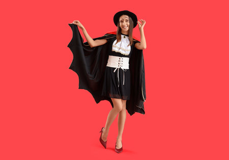 Beautiful young happy woman dressed as vampire for Halloween on red backgroundの写真素材