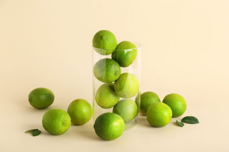 Glass with fresh ripe limes on beige background