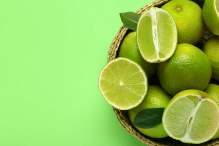 Wicker basket with fresh ripe limes and leaves on green background