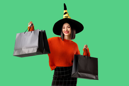 Beautiful young happy woman dressed as witch for Halloween with shopping bags on green backgroundの写真素材