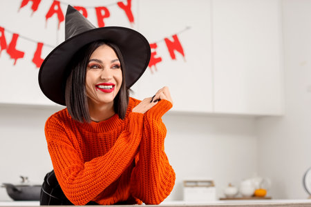 Beautiful young happy woman dressed as witch for Halloween in kitchenの写真素材