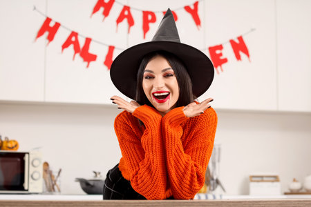 Beautiful young happy woman dressed as witch for Halloween in kitchenの写真素材