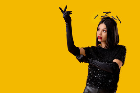 Beautiful young woman in bats headband dressed for Halloween on yellow background