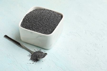 Bowl and spoon with poppy seeds on light blue background, closeupの写真素材