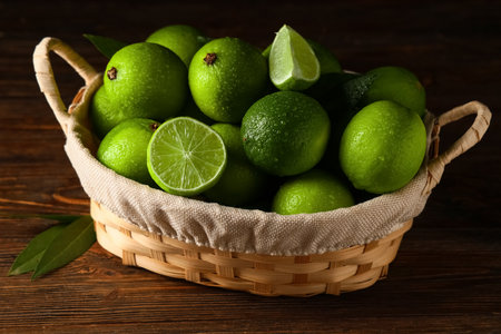Wicker basket with fresh ripe limes on wooden backgroundの写真素材